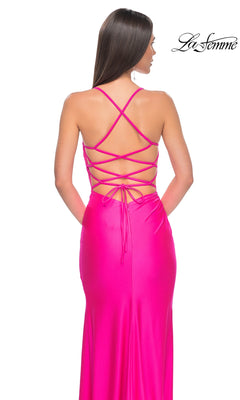 A woman faces away from the camera, wearing the La Femme Strappy Open-Back Long Prom Dress 31129 in bright pink with a lace-up open back and crisscross straps. The La Femme logo is in the top right corner.