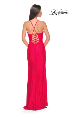 A woman models the La Femme Corset-Back Long Prom Dress 31131, a fitted, floor-length gown in bright red with a crisscross lace-up open back. She faces away from the camera, highlighting the elegant corset-inspired design.