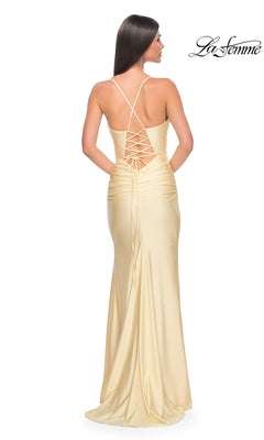 Woman wearing the La Femme Corset-Back Long Prom Dress 31131 in light yellow, featuring a lace-up open back and thin crisscross straps, stands facing away from the camera. "La Femme" logo appears in the top right corner.