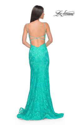 A woman wearing the La Femme Long Floral-Lace Prom Dress 31134, which features turquoise floral lace, a low open back, and thin crisscross straps, stands facing away from the camera.