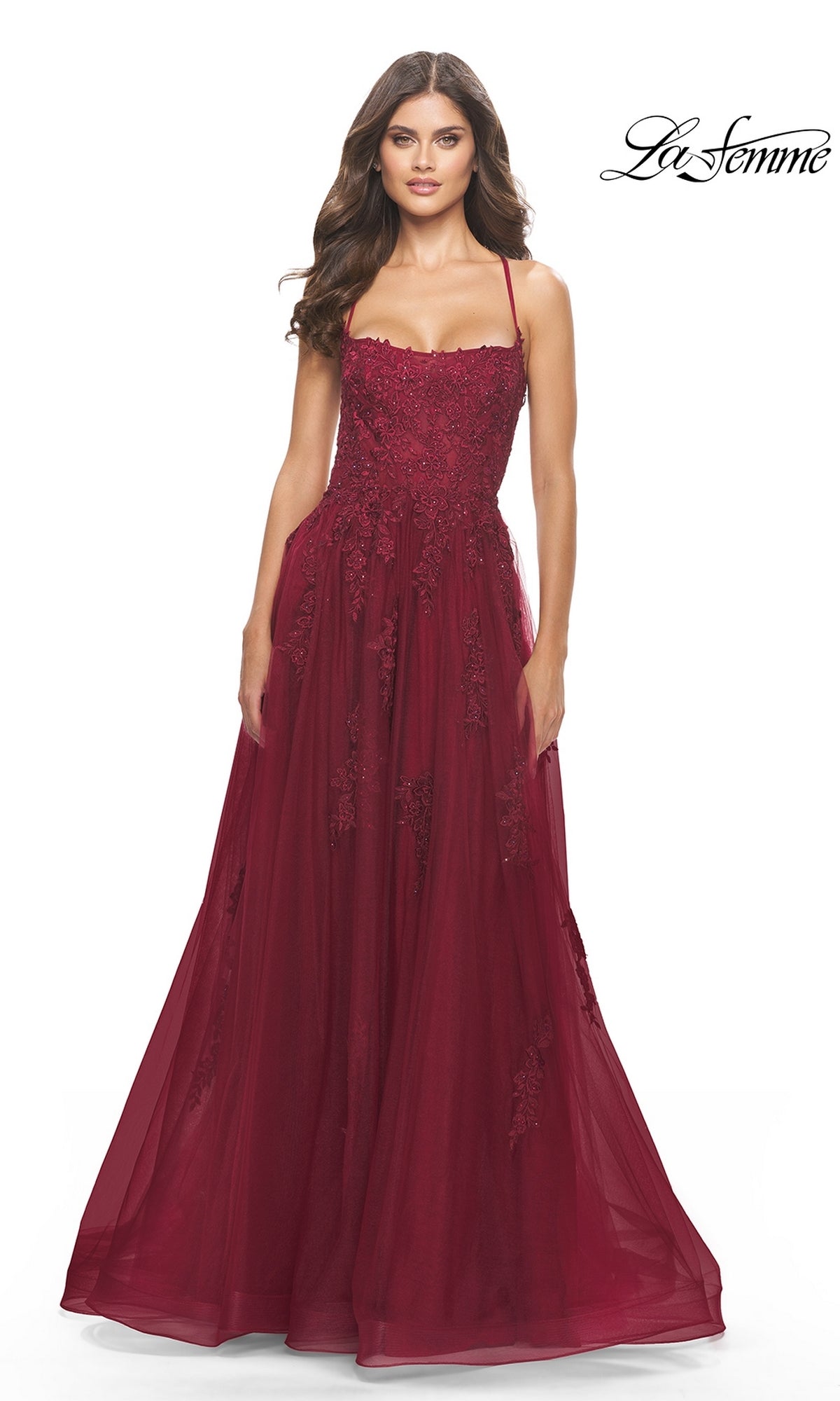 A woman models the La Femme Long A-Line Lace Prom Ball Gown 31135— a sleeveless, floor-length burgundy embroidered lace dress with thin straps and a fitted bodice—against a white background.