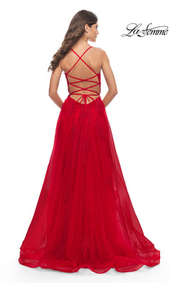 A woman stands with her back to the camera wearing the La Femme Long A-Line Lace Prom Ball Gown 31135, a red formal dress featuring crisscross lace-up straps and an open-back design. The La Femme logo appears in the top right corner.