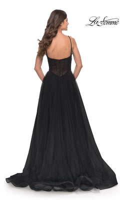 A woman faces away, showcasing the sheer back and flowing skirt of the Sheer-Waist La Femme Long Prom Ball Gown 31147, a black, floor-length dress with thin straps. The La Femme logo appears in the top right corner.