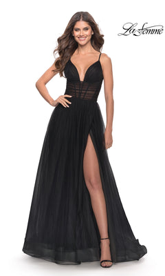 A woman wears the Sheer-Waist La Femme Long Prom Ball Gown 31147 in black, featuring a sleeveless design, deep V-neckline, sheer bodice, high slit, and floor-length skirt, standing against a white background.