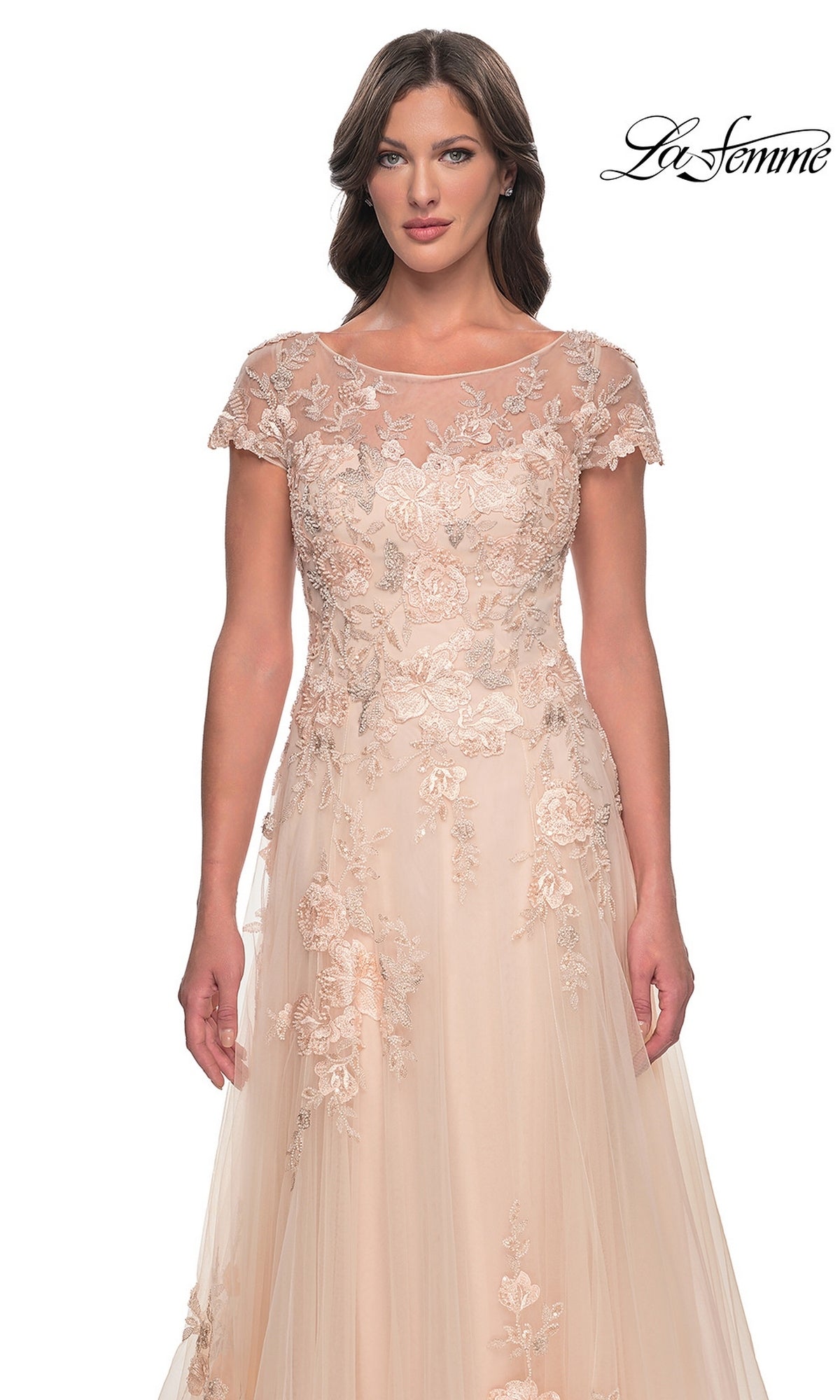 A woman wearing the Long Formal Dress: La Femme 31198, a champagne formal dress featuring a blush-colored A-line tulle skirt, a sheer illusion neckline, cap sleeves, and floral embroidery.