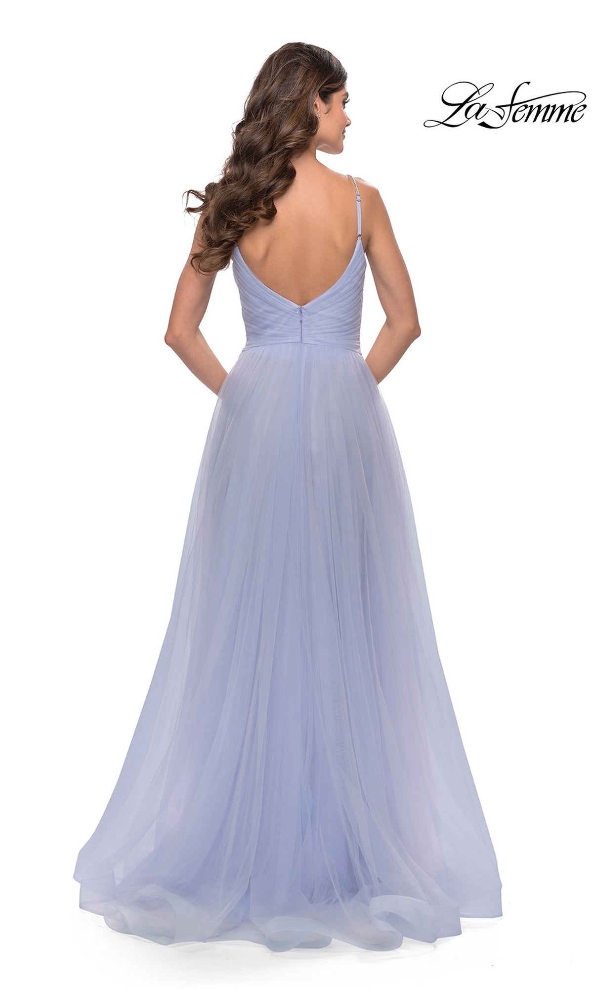 A woman stands facing away in the La Femme A-Line Long Tulle Prom Dress 31204, a floor-length light purple gown with thin straps, low back, and flowing layers of ethereal tulle.
