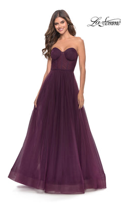 A woman stands smiling against a white background, wearing the Strapless Long Prom Ball Gown: La Femme 31205 in dark purple, featuring a fitted bodice and a tulle A-line ball gown skirt.