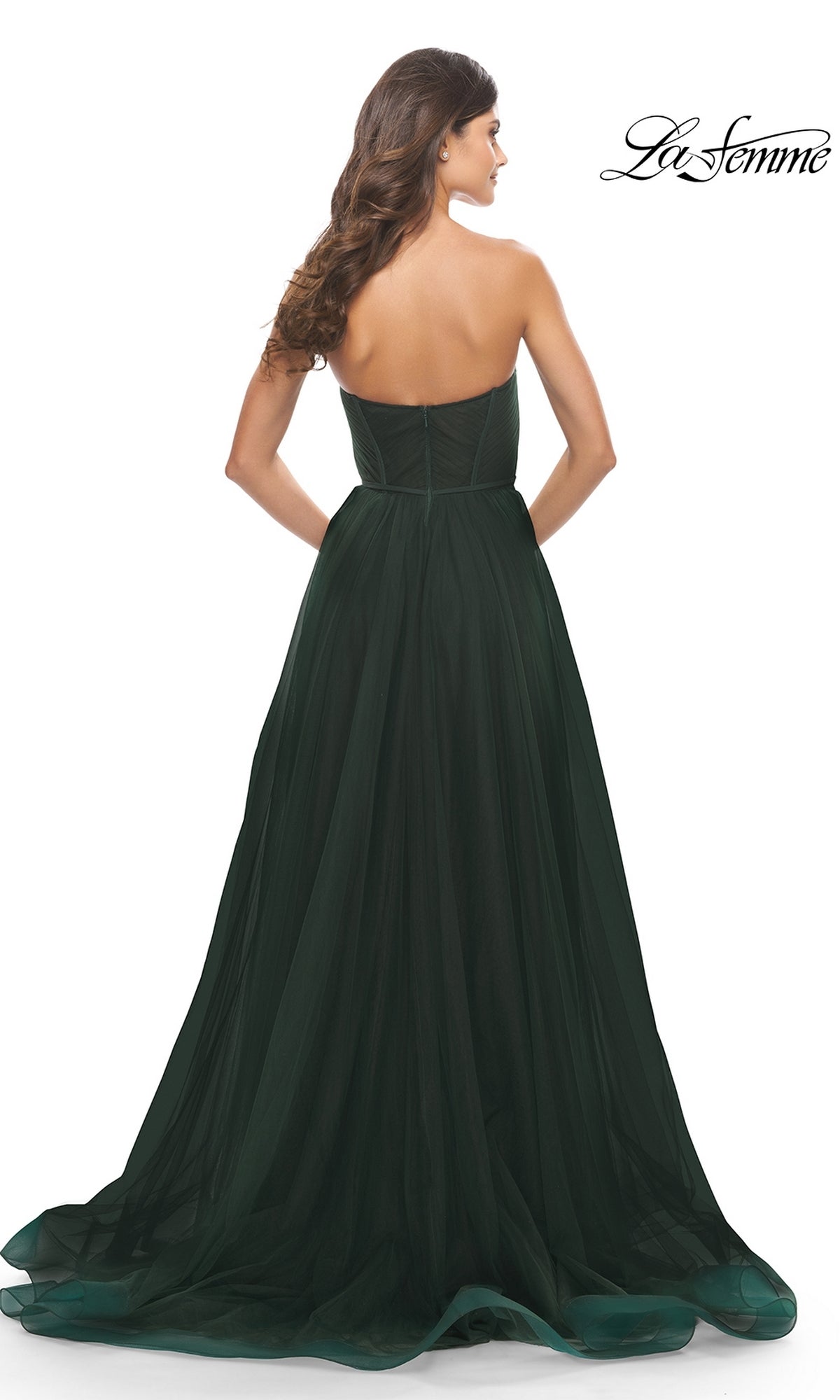 A woman wears the Strapless Long Prom Ball Gown: La Femme 31205, a floor-length dark green dress with a fitted bodice and flowing A-line skirt. 