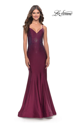 A woman stands smiling in the V-Neck Open-Back La Femme Shimmer Prom Dress 31220, a sleeveless burgundy floor-length gown with a fitted bodice and subtle sparkle.