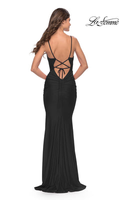 Woman wearing the Simple V-Neck La Femme Designer Prom Dress 31227, a long black fitted gown with thin straps, ruching, and a lace-up open back, poses facing away from the camera.