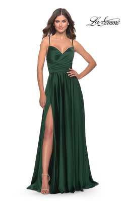 A woman stands against a white background wearing the La Femme Open-Back A-Line Designer Prom Dress 31233, a dark green satin gown with spaghetti straps, fitted bodice, high leg slit, and floor-length skirt exuding elegance.