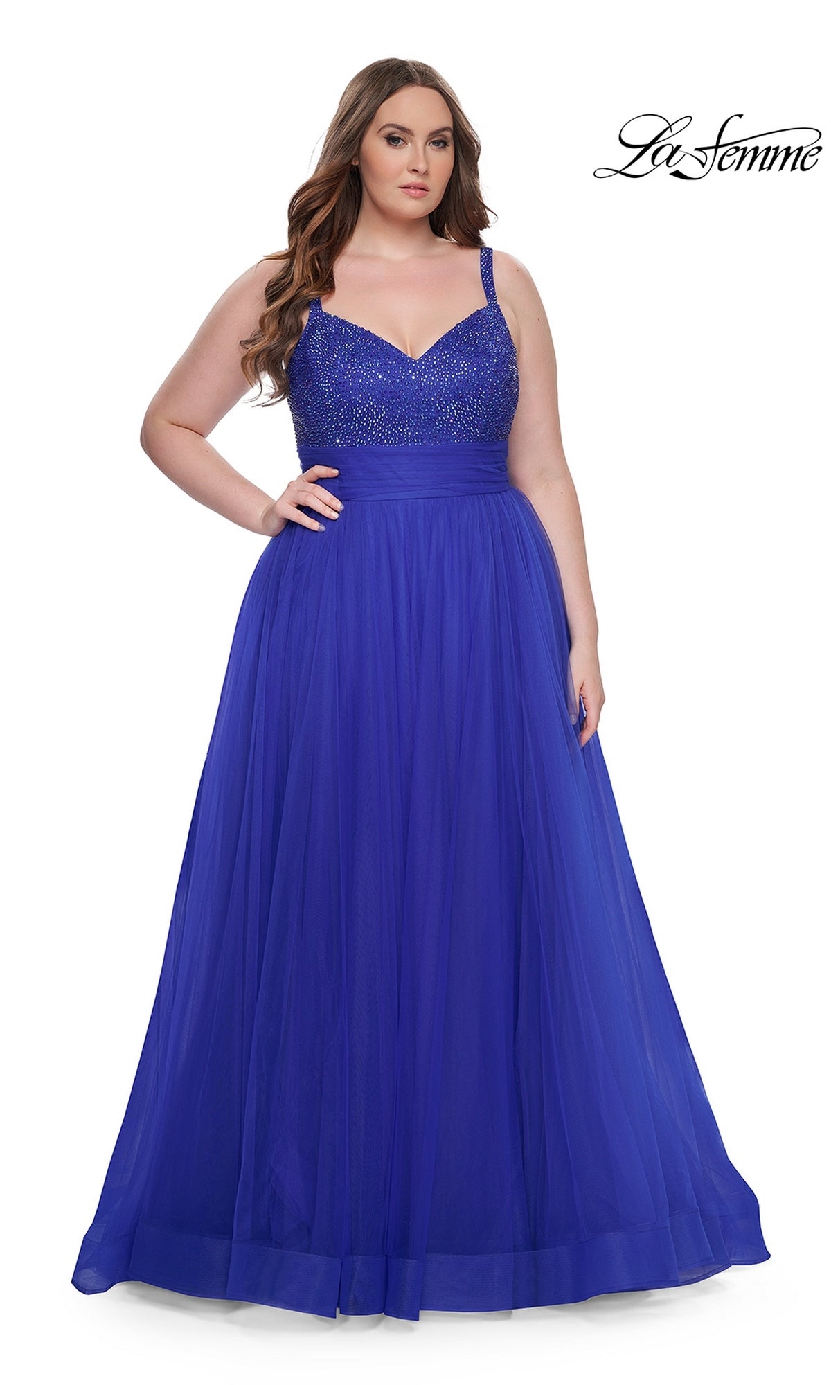A woman models the La Femme Long Prom Dress 31251, a plus-size, floor-length deep blue gown with a beaded bodice and tulle skirt, standing against a white background. The 