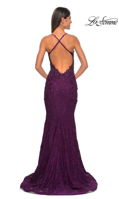 A woman stands with her back to the camera in the La Femme Beaded-Lace Long Prom Dress 31265, a deep purple fitted mermaid gown featuring beaded lace, a low open back with crisscross straps, and a slight train.