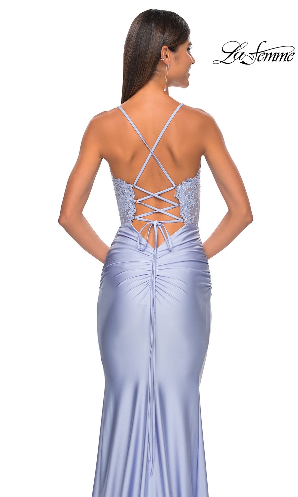 A woman models the La Femme Sheer-Corset Tight Long Prom Dress 31272 in light blue, featuring satin fabric, lace-up back detail, and crisscross straps, standing with her back to the camera.