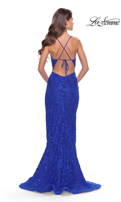 A woman stands facing away in the La Femme Open-Back Long Lace Prom Dress 31288, a fitted, floor-length royal blue gown with floral lace, thin crisscross straps, and an open back.