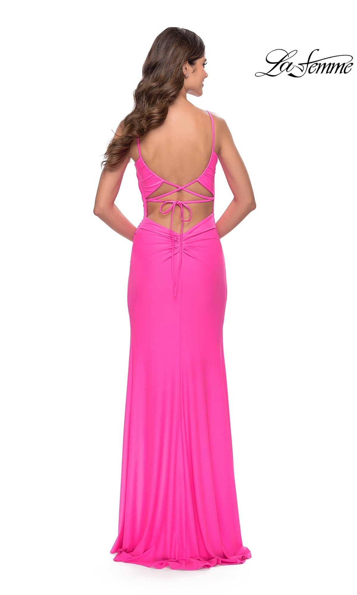 A woman models the La Femme Side-Slit Backless Long Prom Dress 31329 in bright pink, featuring thin straps, lace-up back detailing, and a floor-length design. The 