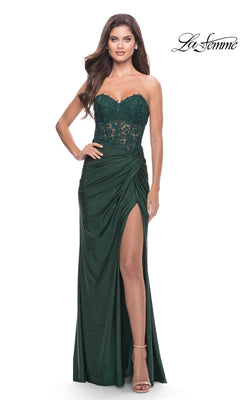 A woman wearing the La Femme Strapless Sheer-Waist Prom Dress 31343 in dark green, featuring a lace bodice with sparkling details, ruched skirt, and thigh-high slit stands with one hand on her hip.