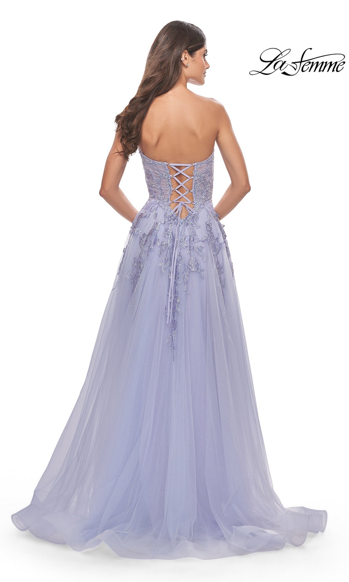 A woman in the La Femme Strapless Sweetheart Long Prom Dress 31363, with floral appliqués, faces away to show off its elegant lace back details.
