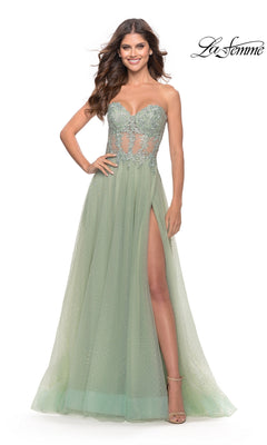 Wearing the La Femme Strapless Sheer-Waist Prom Dress 31367 in mint green, a woman showcases its lace-embroidered sheer bodice, floral details, thigh-high slit, and floor-length A-line tulle skirt with one hand on her hip.