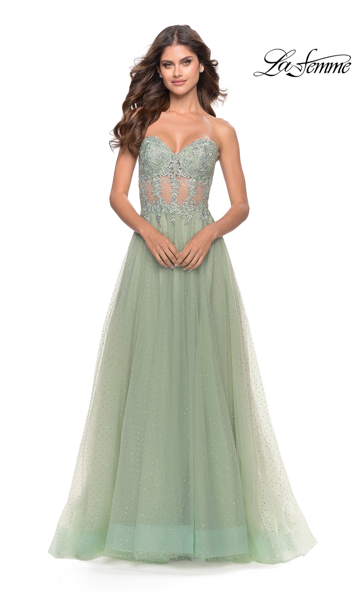 A woman models the La Femme Strapless Sheer-Waist Prom Dress 31367, a pale green gown with a sheer lace-embroidered bodice and flowing A-line tulle skirt. The 