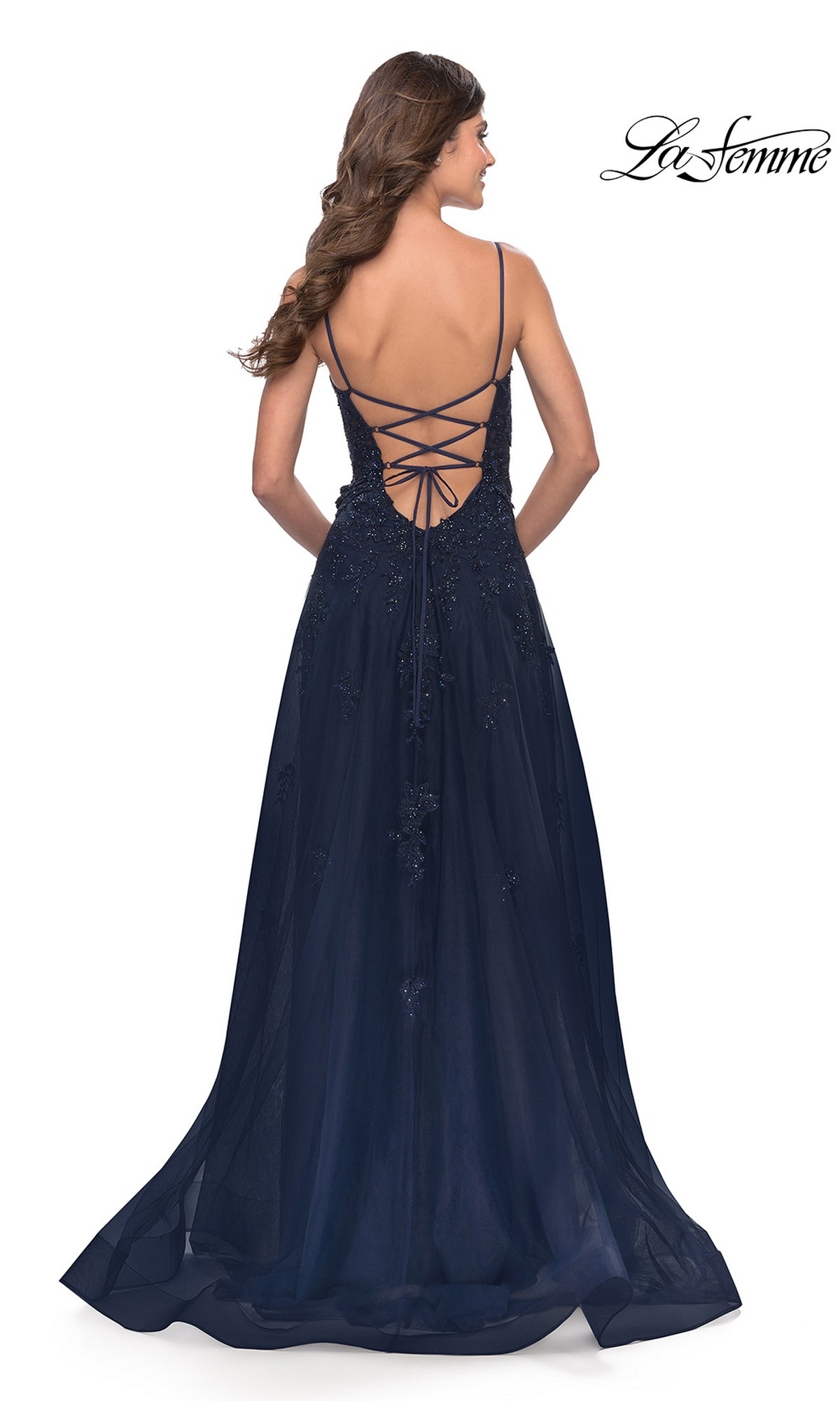 A woman stands facing away from the camera in the La Femme Lace-Bodice Long A-Line Prom Dress 31381, featuring a navy blue embroidered lace bodice with beaded details and a lace-up open back.