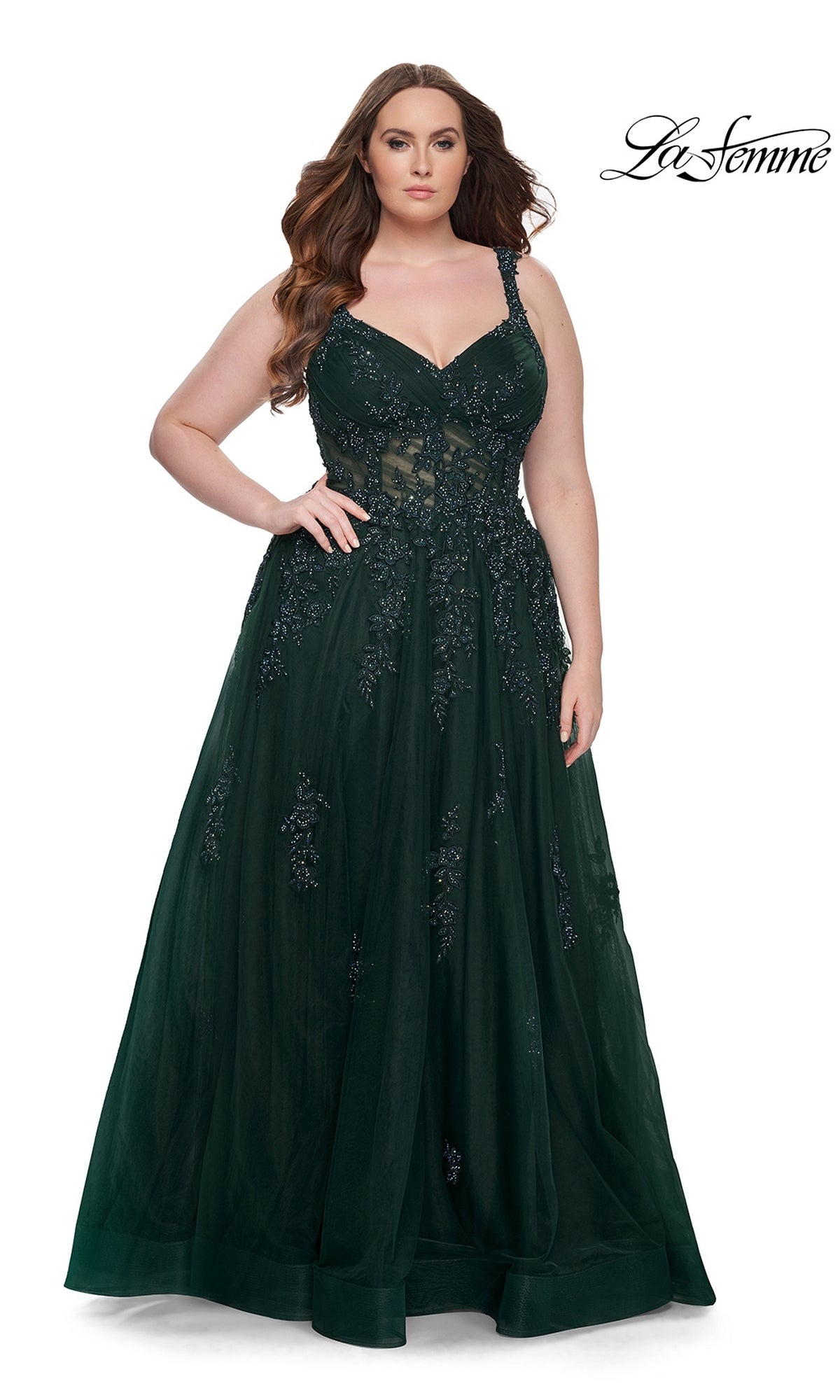 A woman stands against a white background wearing the La Femme Long Prom Dress 31383, a dark green, floor-length sleeveless lace gown with floral embroidery. The 
