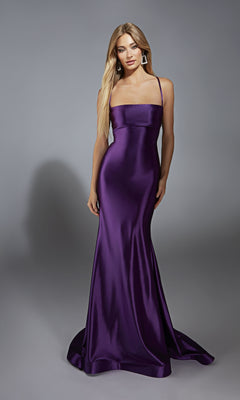 A woman poses against a gray background in the Aerie Couture 313, a floor-length, sleeveless satin prom dress in purple with lace-up open back, thin straps, and geometric earrings.
