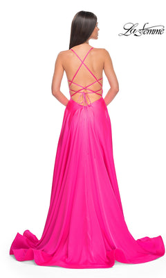 A woman with straight brown hair wears the La Femme Neon Pink Long Prom Dress 31448, featuring a beaded bodice, crisscross open back, and flowing floor-length train.