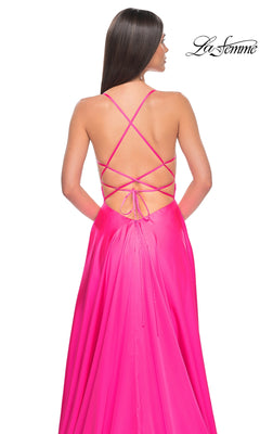 A woman wears the La Femme Neon Pink Long Prom Dress 31448, featuring a beaded bodice, open back, and crisscross lace-up straps, standing against a white background with the "La Femme" logo in the top right corner.