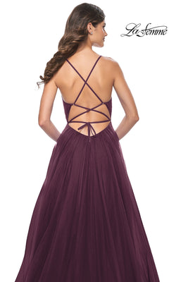 A woman wears the La Femme Sheer-Waist Long Prom Ball Gown 31457, a floor-length, sleeveless dark purple dress with crisscross straps and an open back. The La Femme logo is displayed in the top right corner.