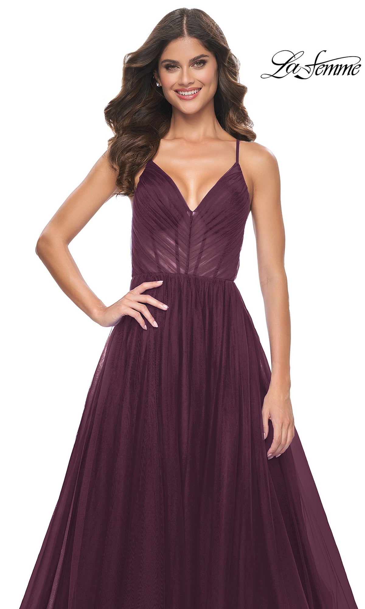 A woman stands smiling against a white background, modeling the La Femme Sheer-Waist Long Prom Ball Gown 31457—a sleeveless, deep purple designer dress with a fitted bodice and flowing skirt. The 