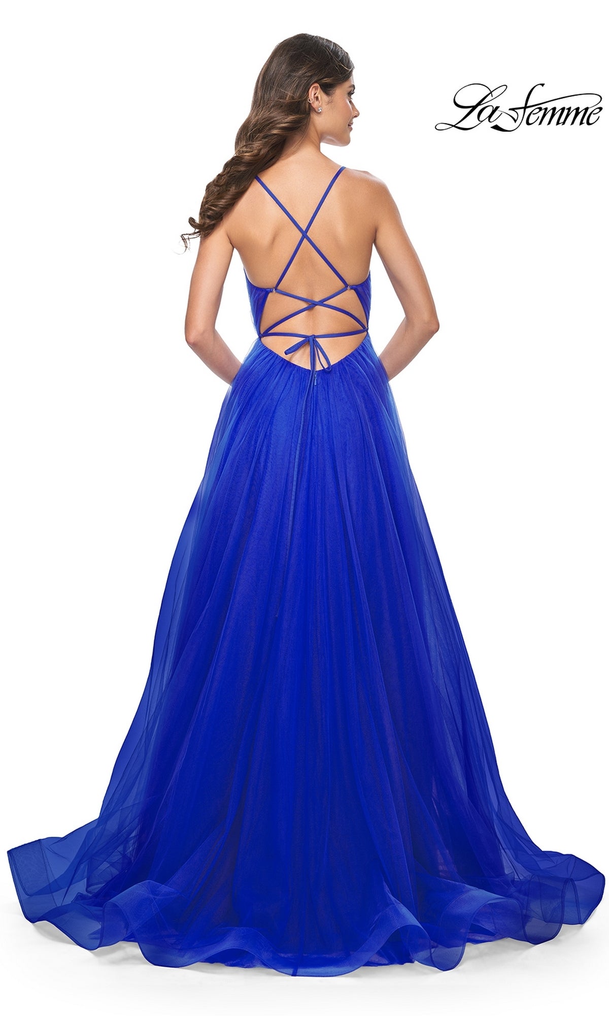 A woman faces away in a bright blue La Femme Sheer-Waist Long Prom Ball Gown 31457, featuring an a-line silhouette, strappy open back, and flowing tulle floor-length skirt.