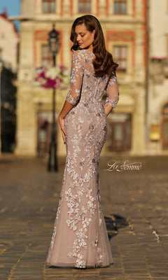 A woman stands outdoors in the La Femme 31464 long formal dress, featuring three-quarter sleeves and detailed floral lace embroidery. Facing away, she highlights the gown's elegant back.