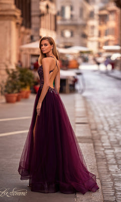 A woman wearing the La Femme Beaded-Bodice Long A-Line Prom Gown 31471 with a sleeveless, v-neck beaded bodice and sheer skirt stands on a city street, looking over her shoulder.