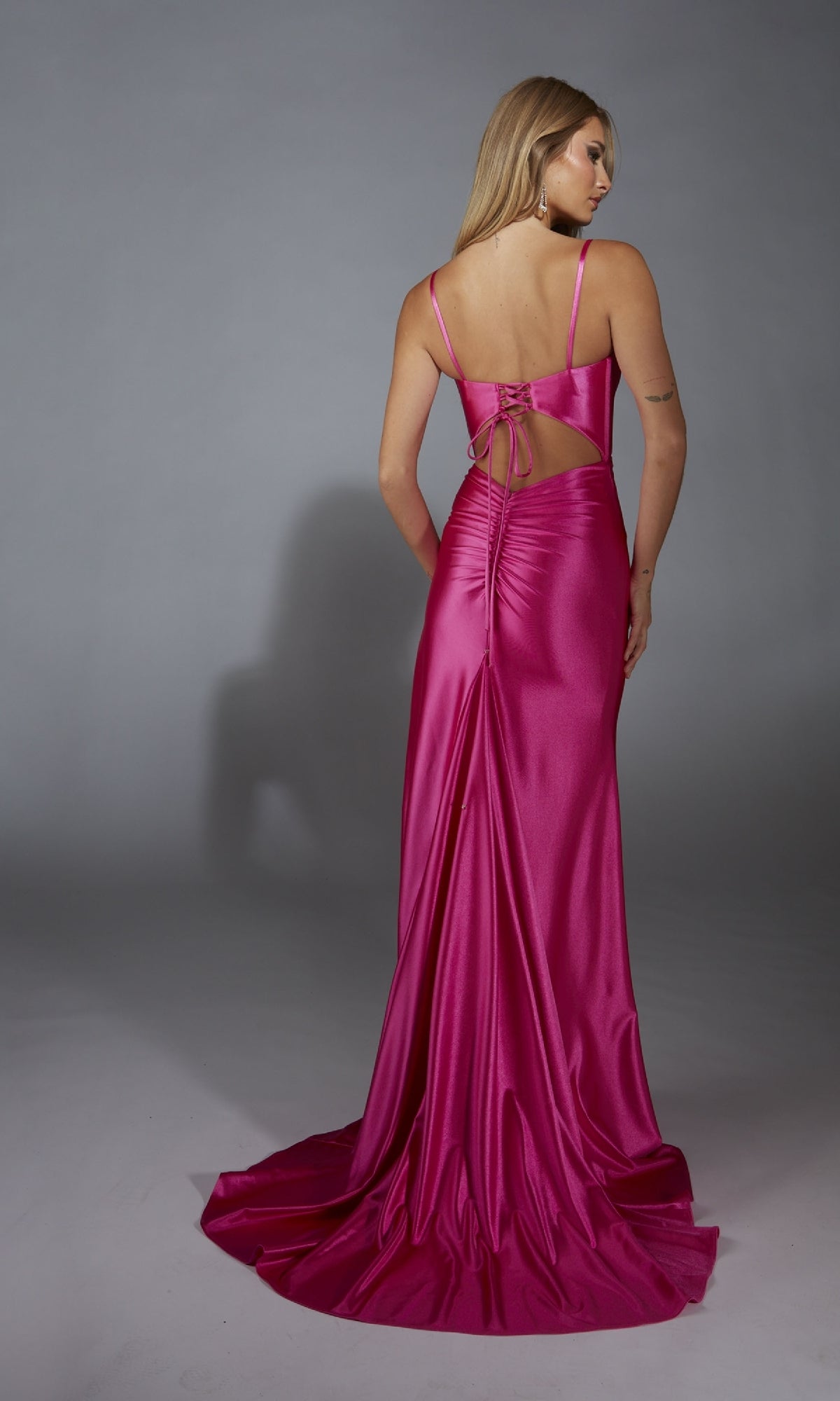 A woman models the Aerie Couture 314, a satin hot pink long formal dress with thin straps, open tie-back, form-fitting silhouette, and subtle side slit, standing against a plain gray background.