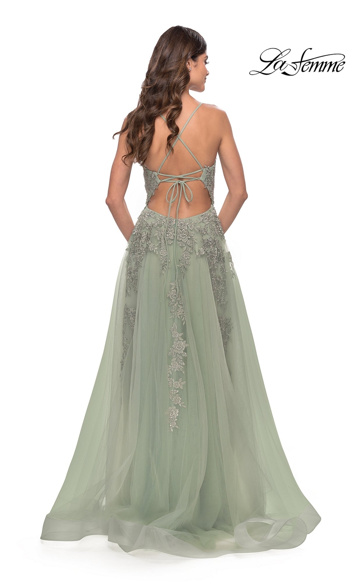 A woman wearing the La Femme Strappy-Back Long A-Line Prom Dress 31503 in sage green, featuring lace detailing and crisscross strappy-back straps, stands facing away from the camera.