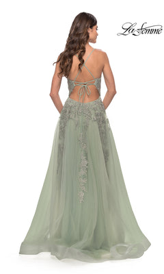 A woman wearing the La Femme Strappy-Back Long A-Line Prom Dress 31503 in sage green, featuring lace detailing and crisscross strappy-back straps, stands facing away from the camera.