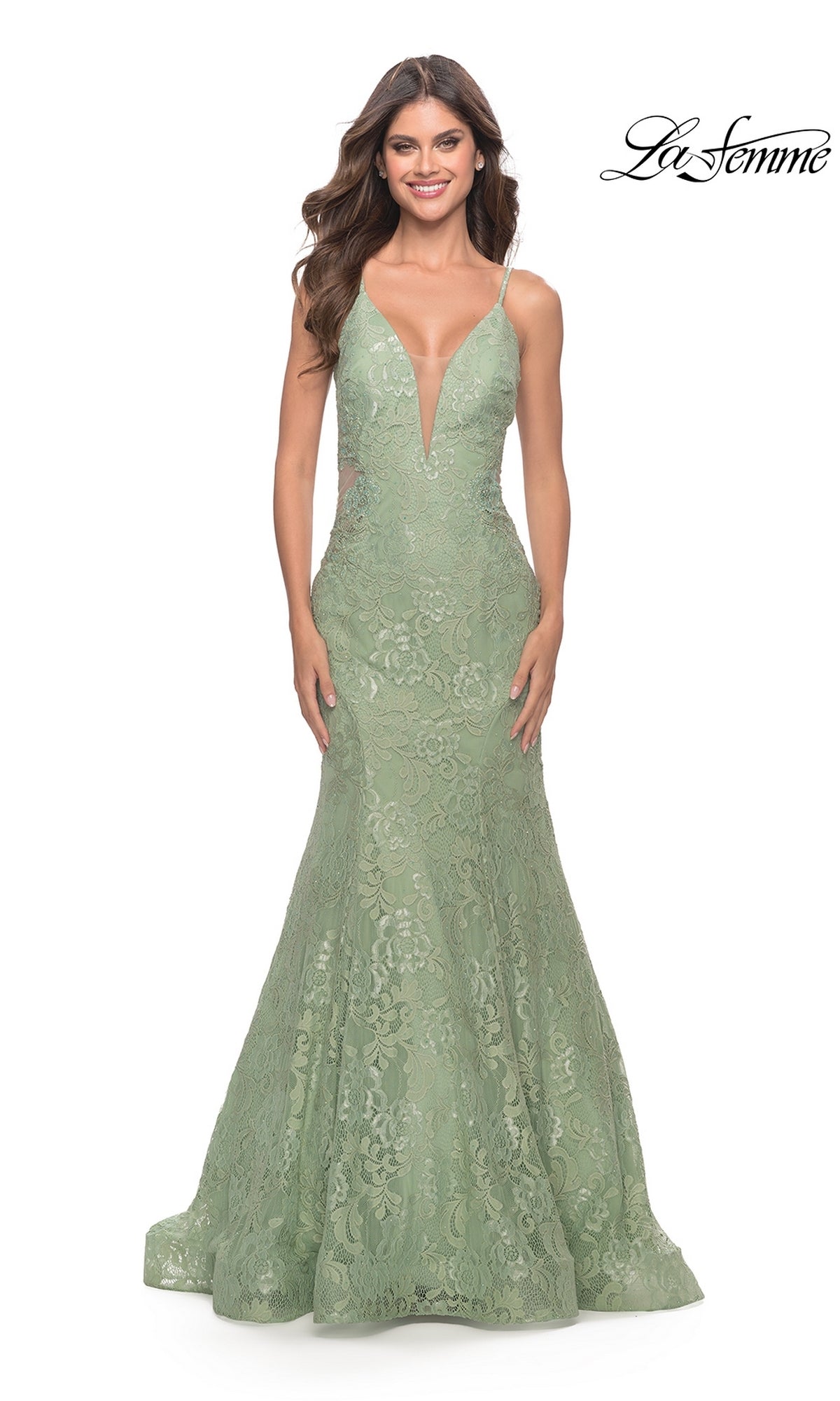 A woman wears the Long Lace Mermaid Prom Dress: La Femme 31512 in sage green, featuring a deep V neckline and thin straps, standing against a white background. The 