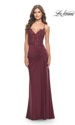 A woman wears the La Femme Long Prom Dress 31520—a sleeveless burgundy gown with a lace embroidered bodice, draped skirt, and twist knot detail—standing against a plain white background. The "La Femme" logo appears in the top right corner.