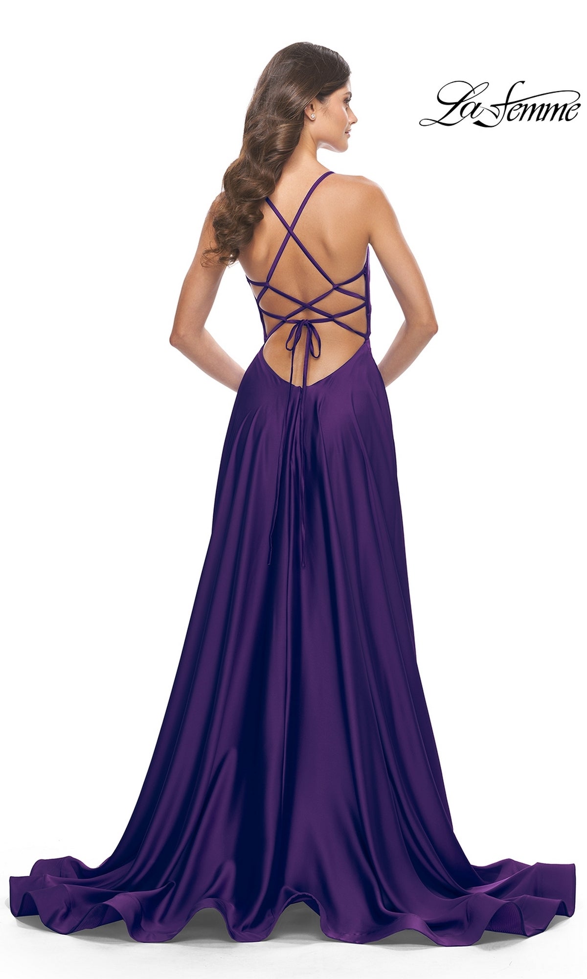 A woman stands facing away, wearing the La Femme 31533 Deep V-Neck Long A-Line Prom Dress—a floor-length purple gown with an open back and crisscross lace-up straps.