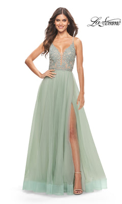 A woman wearing the Lace-Bodice Long A-Line Prom Dress La Femme 31542, featuring a light green hue, embroidered lace bodice, sheer skirt with high slit, and spaghetti straps, stands smiling against a white background.
