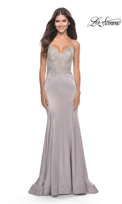 A woman wears the La Femme Long Prom Dress 31555, featuring a lilac lace bodice, silver embellishments, and spaghetti straps, standing against a white background.
