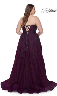A woman in the La Femme Long Prom Dress 31570, a plus-size strapless purple ball gown with a corset-style bodice and lace-up back, stands facing away from the camera in a floor-length design.