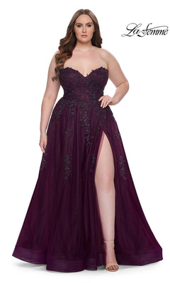 A woman in the La Femme Long Prom Dress 31570, a plus-size strapless gown with a corset bodice, floral embellishments, and a high leg slit, stands against a white background.