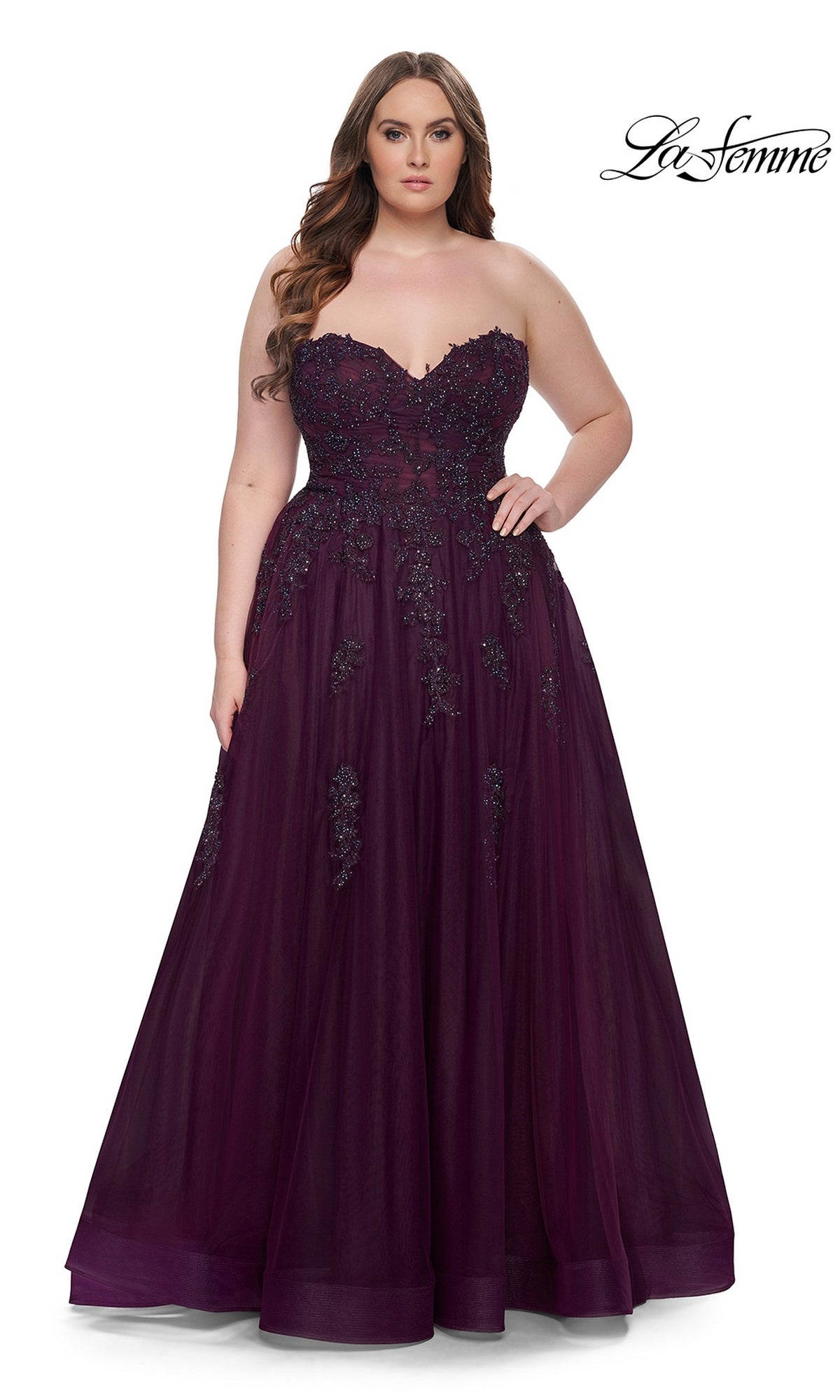 A woman models the La Femme Long Prom Dress 31570, featuring a plus-size strapless design with a corset-style bodice and embroidered lace, standing facing forward against a plain white background.