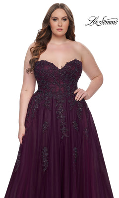 A woman models the La Femme Long Prom Dress 31570, a strapless deep purple gown with black beading and a corset-style bodice, standing against a white background. The La Femme logo appears in the top right corner.