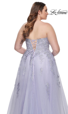 A woman with long brown hair models the La Femme Long Prom Dress 31570, a plus-size strapless gown with a corset-style bodice and floral embroidery, standing against a white background.