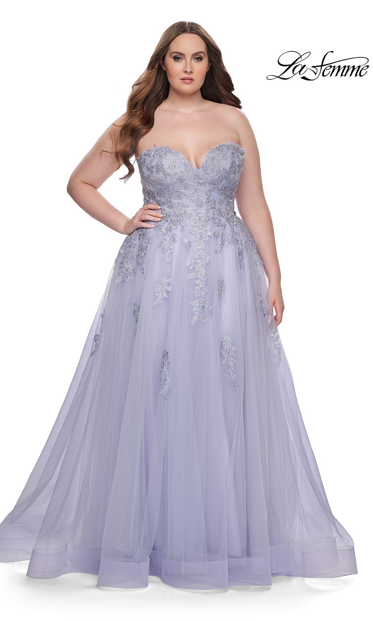 A woman models the La Femme Long Prom Dress 31570, a lavender plus-size strapless gown with silver floral embellishments and a corset-style bodice, standing against a white background.