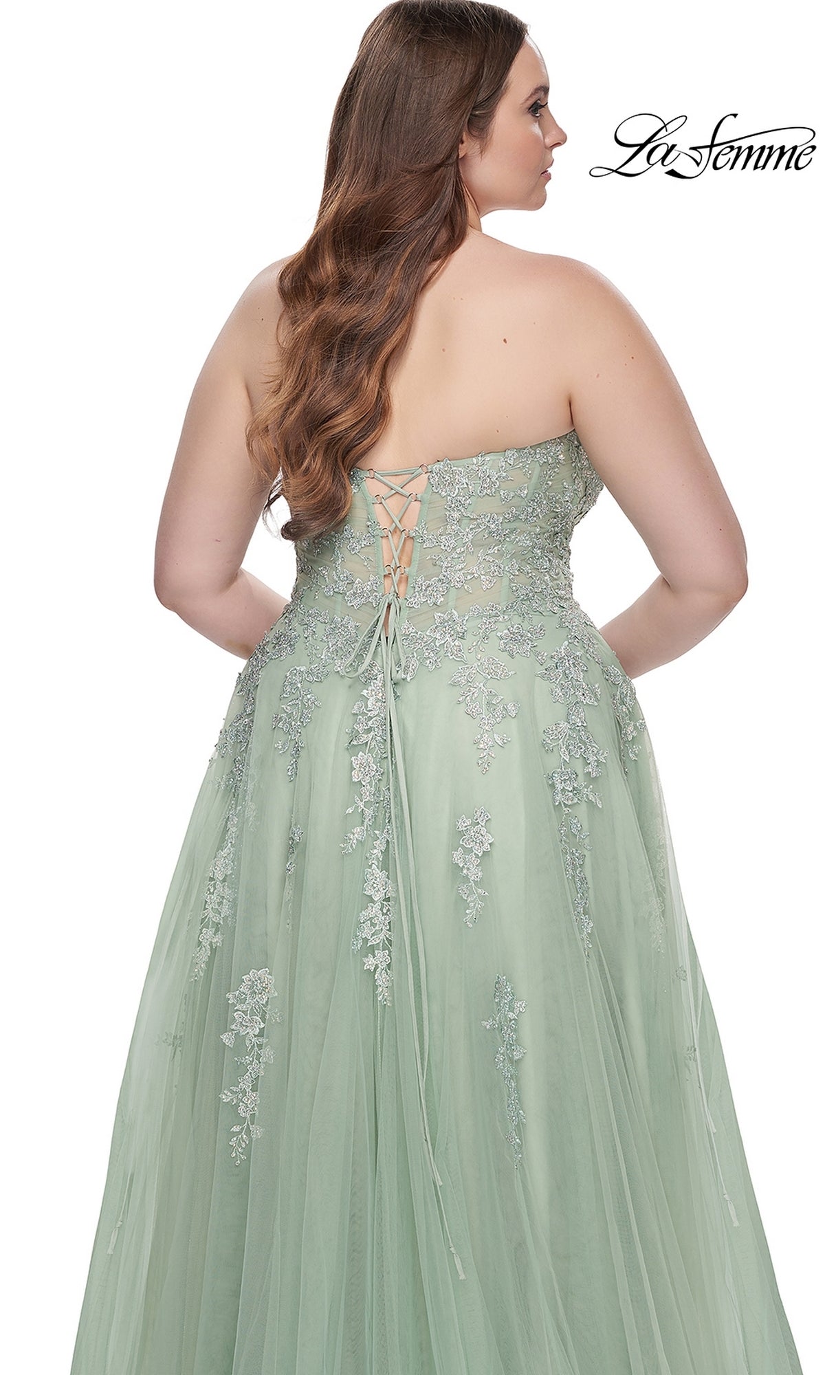 A woman is photographed from behind wearing the La Femme Long Prom Dress 31570, a plus-size strapless light green gown with embroidered lace and a lace-up back.