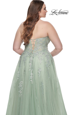 A woman is photographed from behind wearing the La Femme Long Prom Dress 31570, a plus-size strapless light green gown with embroidered lace and a lace-up back.